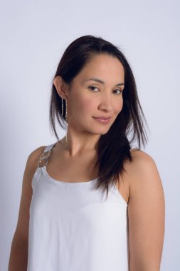 Beyaz elbiseli güzel Venezuelalı bir kadının portresi, haylaz bir şekilde kameraya bakıyor, gülümsüyor ve sakin, barış ve ahengi ifade ediyor, beyaz arka planlı stüdyo fotoğrafı