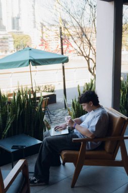 Kısa saçlı ve vitiligolu genç Arjantinli bir adam bir kafede oturmuş dizüstü bilgisayarıyla internette geziniyor.