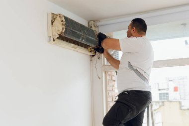 Katlanan alüminyum merdivendeki Latin Adam, dairedeki klimanın elektrik panelini söküyorlar, bakım ve ev hizmetleri kavramını..