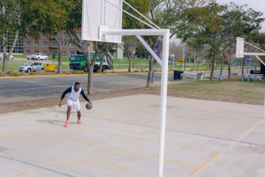 Basketbol sahasında top sürme eğitimi alan beyaz üniformalı genç Afrikalı sporcu, turnuvaya hazırlanıyor..