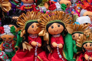 A collection of dolls with gold and green accents. The dolls are smiling and appear to be happy. Historic center of Queretaro City, decorations and traditions to celebrate Mexico's Independence Day, colonial architecture, alleys and facades