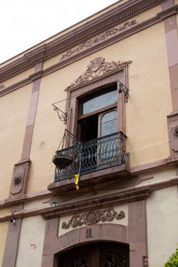 A building with a balcony and a window. The balcony is open and has a yellow object on it. Historic center of Queretaro City, decorations and traditions to celebrate Mexico's Independence Day, colonial architecture, alleys and facades