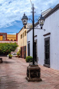 A street with a lamp post and a building with a window. The street is empty and the sky is blue. Historic center of Queretaro City, decorations and traditions to celebrate Mexico's Independence Day, colonial architecture, alleys and facades