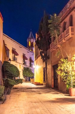 A narrow street with a tall building in the background. The street is lit up at night. Historic center of Queretaro, colonial architecture, decorations for the celebration of Mexico's Independence Day.