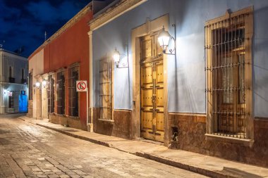 A street with a blue sign that says no smoking. The street is lined with buildings. Historic center of Queretaro, colonial architecture, decorations for the celebration of Mexico's Independence Day.