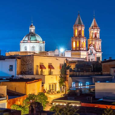 A city at night with a large church in the background. The church is lit up and the sky is dark. Historic center of Queretaro, colonial architecture, decorations for the celebration of Mexico's Independence Day.