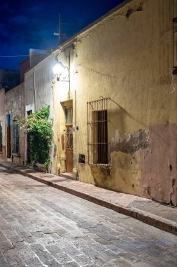 A street at night with a building in the background. The street is empty and the building is yellow. Historic center of Queretaro, colonial architecture, decorations for the celebration of Mexico's Independence Day.