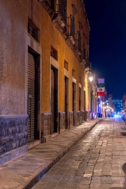 A brick walkway with a few buildings in the background. The buildings are brown. Historic center of Queretaro, colonial architecture, decorations for the celebration of Mexico's Independence Day.