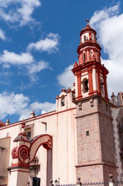 A large red and white building with a tall tower. The building is surrounded by a courtyard. Historic center of Queretaro, colonial architecture, decorations for the celebration of Mexico's Independence Day.