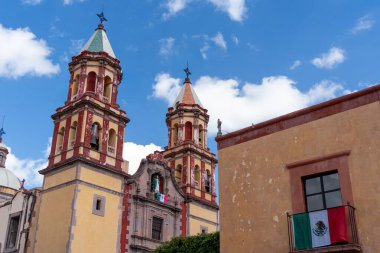 A historic building with two tall towers and a large window. The building is situated in a peaceful. Historic center of Queretaro, colonial architecture, decorations for the celebration of Mexico's Independence Day.