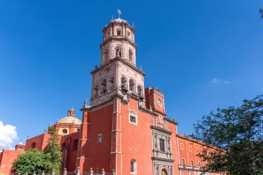 A beautiful red building with a tall tower and a blue sky in the background. Historic center of Queretaro, colonial architecture, decorations for the celebration of Mexico's Independence Day.