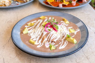 Üstünde beyaz sos ve avokado olan bir tabak yemek. Tabak mavi ve yemek kahverengi. Queretaro 'nun tarihi merkezi, sömürge mimarisi, Meksika' nın Bağımsızlık Günü kutlamaları için dekorasyonlar.