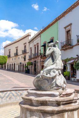 A statue of a woman is placed on top of a fountain in front of a building. Historic center of Queretaro, colonial architecture, decorations for the celebration of Mexico's Independence Day.