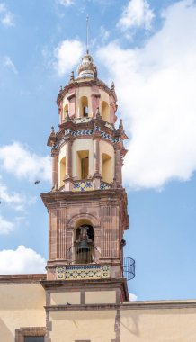 Tepesinde çan olan uzun bir kule. Kule bulutlarla çevrili. Gökyüzü mavi. Queretaro 'nun tarihi merkezi, sömürge mimarisi, Meksika' nın Bağımsızlık Günü kutlamaları için dekorasyonlar.