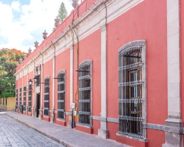 A red building with a yellow roof and a yellow door. The building has a lot of windows and a balcony. Historic center of Queretaro, colonial architecture, decorations for the celebration of Mexico's Independence Day.
