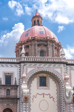 A large pink dome sits atop a building with a blue sky in the background. The building is ornate. Historic center of Queretaro, colonial architecture, decorations for the celebration of Mexico's Independence Day.