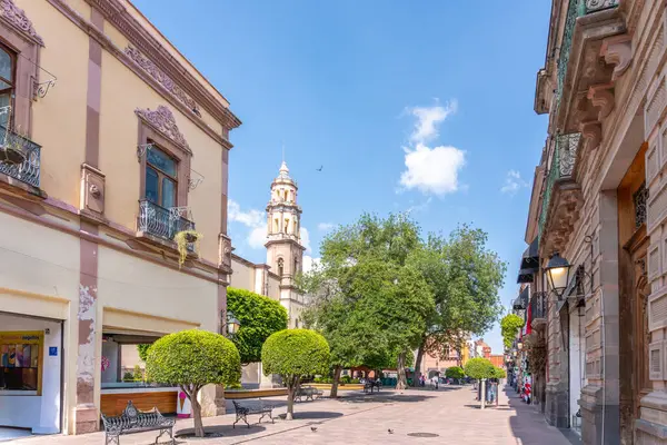 The street is lined with buildings, including a tall one with a church in the middle. Historic center of Queretaro, colonial architecture, decorations for the celebration of Mexico's Independence Day.