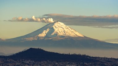 Üzerinde kar olan bir dağ bir şehrin arka planındadır. Dağ çok yüksektir ve şehir çok küçüktür. Mexico City 'nin panoramik manzarası, karla kaplı volkanlar Popocatepetl ve Iztaccihuatl!