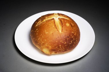 Yuvarlak zanaatkar ekmeği haç kesimi ile beyaz bir tabakta servis edilir Gradien arka planda koyu