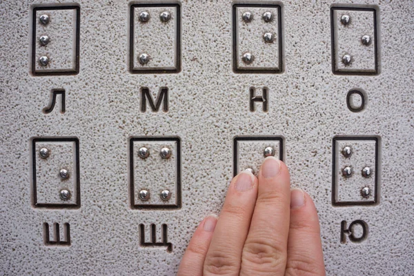 Woman\'s hand is reading Braille outdoors close-up. Tactile reading of the letters of the Ukrainian alphabet (Cyrillic) in Braille in a public park