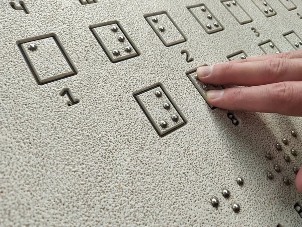 The hand of a person with blindness is reading the Braille outdoors, touching the relief. Close-up of hand is reading a Braille sign. Concept of World Sight Day. World Braille Day. Concept of the day of the blind and disability. Blindness