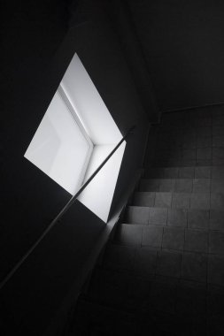 Merdiven manzarası var. Karanlık ışıklı bir merdiven. Işık kaynağı standart olmayan geometrik şekilli (eşkenar dörtgen ya da paralelkenarlı) geniş bir penceredir. Parlak gün ışığı, karanlık iç mekâna güçlü bir zıtlık yaratır. Soyut, minimalist görünüm