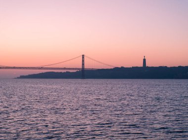 Lizbon, Portekiz 'deki 25 de Abril köprüsünün hava gündoğumu görüntüsü. Belem Kulesi 'nin bitişiğindeki kamu malından çekilmiş.
