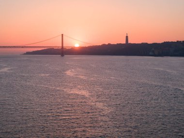 Lizbon, Portekiz 'deki 25 de Abril köprüsünün hava gündoğumu görüntüsü. Belem Kulesi 'nin bitişiğindeki kamu malından çekilmiş.
