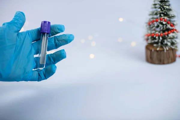 Vacuum blood collection tube with sodium citrate in blue gloves for laboratory. Test tube with blurred christmas tree and lights in background