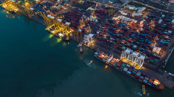 aerial top view international shipping port load and unloading container by crane onto transport ships and trailer for import export distributing products to customers and consumer over lighting at night scene shot