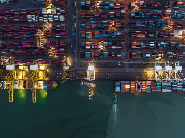 aerial top view international shipping port load and unloading container by crane onto transport ships and trailer for import export distributing products to customers and consumer over lighting at night scene shot