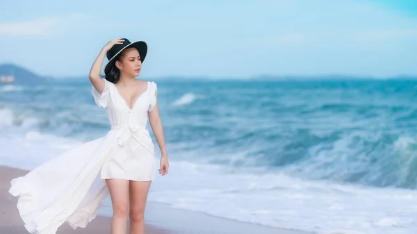 年轻的亚洲女性游客身穿白衣 头戴黑帽 在海滩上悠闲自在地散步 享受着大海和快乐的暑假 — 图库照片