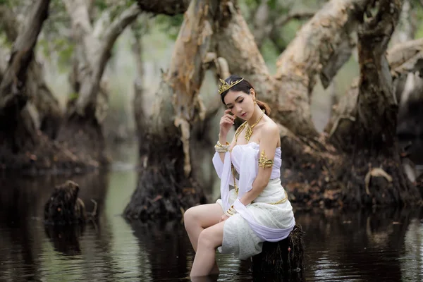 美丽动人的泰籍亚洲女人穿着白色的当地传统服装 名字叫Nakee 坐在湖边的树桩上 在植物园里 Rayong Thailand Nakee Portait模型在公园里的概念 — 图库照片