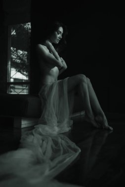 black and white portrait model asian women naked sitting with some white cloth in dark room, emotion of art natural light and shadow concept 
