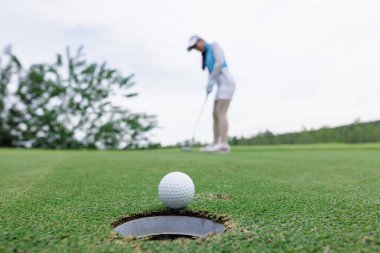asian woman golf player putting successfully ball on green, close up selective focus blur background and clear sky, wide angle shot