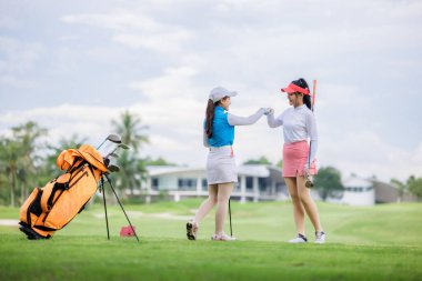 two asian women golfers congratulate high-five and happy smiling at golf course, with the golf bag next to them, sport women professional golfer concept,