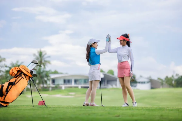two asian women golfers congratulate high-five and happy smiling at golf course, with the golf bag next to them, sport women professional golfer concept,