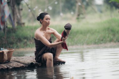 Asyalı kadın salonda oturuyor, ahşap köprüde oturuyor, nehirde giysileri yıkıyor, elbiseleri yıkıyor ve Asyalı tarzı seksilik kavramını uyguluyor.