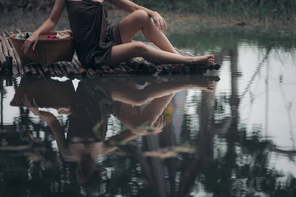 川で木橋の洗濯服に座ってサロンを身に着けているアジアの女性 洗濯服やセクシーなアジアスタイルの概念 — ストック写真