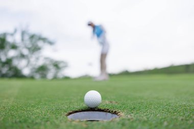 asian woman golf player putting successfully ball on green, close up selective focus blur background and clear sky, wide angle shot