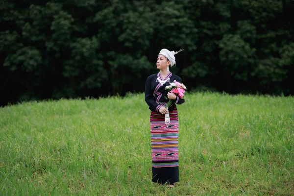 アジアの若い女性の自然光の肖像画は 伝統的なタイの文化ランナのドレススタイルと自然の庭 森の背景に彼女の手で花を身に着けている緑の草の上に立っています — ストック写真