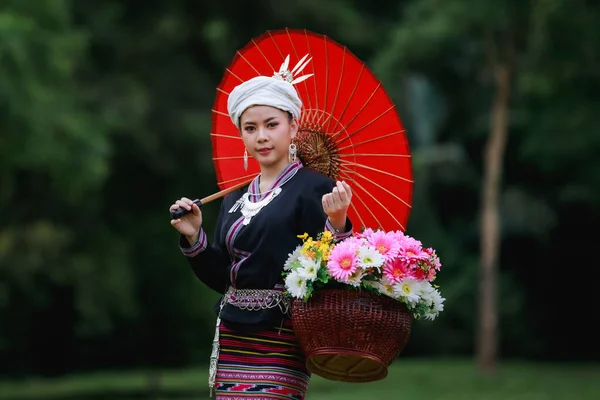 伝統的なタイの文化ランナのドレススタイルと花のバスケットと自然の庭 森の背景に彼女の赤い傘を身に着けているアジアの若い女性の肖像画 — ストック写真
