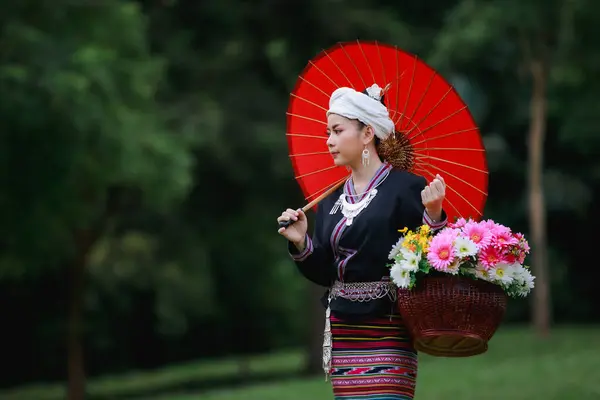 亚洲年轻女子的画像 站在绿草上 身穿传统的泰族文化长裙 穿着花篮和红色的雨伞 在自然的花园 森林的背景 — 图库照片
