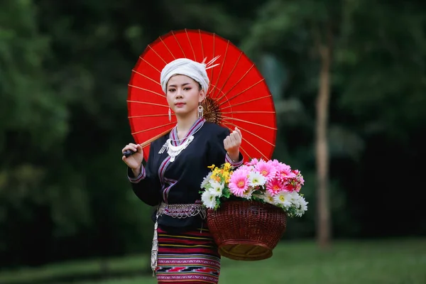 伝統的なタイの文化ランナのドレススタイルと花のバスケットと自然の庭 森の背景に彼女の赤い傘を身に着けているアジアの若い女性の肖像画 — ストック写真