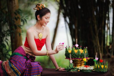  Geleneksel Tayland kırmızı elbiseli güzel bir kadının portresi elinde çiçekle oturur ve krathong 'u Loy Krathong Günü' nde siyah arka planda süslerdi.,