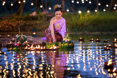 Loi Krathong Festivali, Taylandlı bir kadın nehir kenarında bir salda oturmuş krathong tutuyor, geleneksel Tayland kostümlü Asyalı kadınlar Loi Krathong Günü, gelenekler ve Tayland kültüründe yüzmek üzere kratonglar getiriyor.