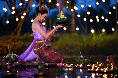 Loi Krathong Festivali, Taylandlı bir kadın nehir kenarında bir salda oturmuş krathong tutuyor, geleneksel Tayland kostümlü Asyalı kadınlar Loi Krathong Günü, gelenekler ve Tayland kültüründe yüzmek üzere kratonglar getiriyor.