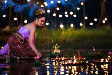Loi Krathong Festivali, Taylandlı bir kadın nehir kenarında bir salda oturmuş krathong tutuyor, geleneksel Tayland kostümlü Asyalı kadınlar Loi Krathong Günü, gelenekler ve Tayland kültüründe yüzmek üzere kratonglar getiriyor.