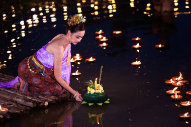 Loi Krathong Festivali, Taylandlı bir kadın nehir kenarında bir salda oturmuş krathong tutuyor, geleneksel Tayland kostümlü Asyalı kadınlar Loi Krathong Günü, gelenekler ve Tayland kültüründe yüzmek üzere kratonglar getiriyor.
