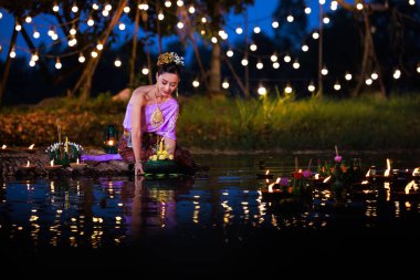 Loi Krathong Festivali, Taylandlı bir kadın nehir kenarında bir salda oturmuş krathong tutuyor, geleneksel Tayland kostümlü Asyalı kadınlar Loi Krathong Günü, gelenekler ve Tayland kültüründe yüzmek üzere kratonglar getiriyor.